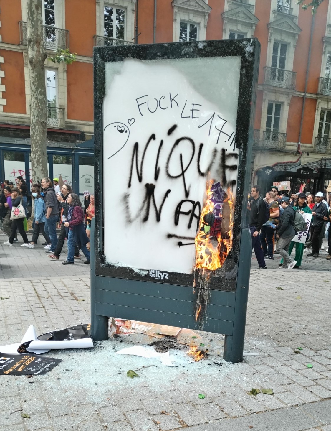 Burning streetsign with graffiti that reads 'Fuck le 17' and 'Nique un fa'